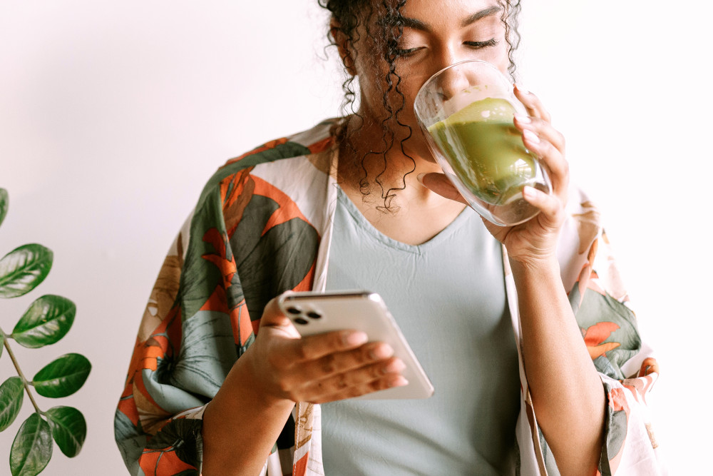 Woman drinking green juice looking at phone